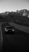 An influencer filming a high-performance car on a winding mountain road at dusk.