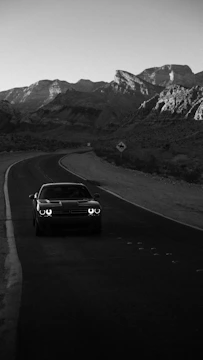An influencer filming a high-performance car on a winding mountain road at dusk.