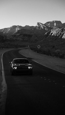 Nighttime shot of a sleek car driving on a mountain road with twinkling village lights.