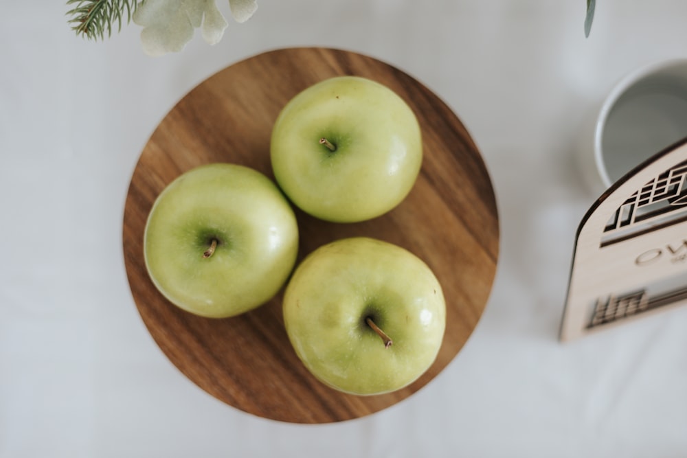 three green apples sitting on a wooden plate