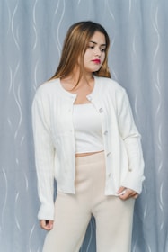 A model wearing a soft, oversized beige cardigan standing against a muted stone wall, embodying comfort and simplicity.