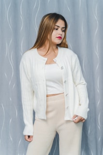 A model wearing a soft, oversized beige cardigan standing against a muted stone wall, embodying comfort and simplicity.