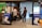 A modern office setting features several people engaging in conversation. Posters advertising Jotform SIGN are prominently displayed on the walls and partitions. The space includes brick walls and large windows, with some natural light coming through. Balloons are in the background, adding a celebratory or casual atmosphere. The individuals are casually dressed, lending a relaxed tone to the environment.