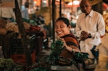 A smiling woman showcasing handcrafted jewelry at a vibrant market stall.