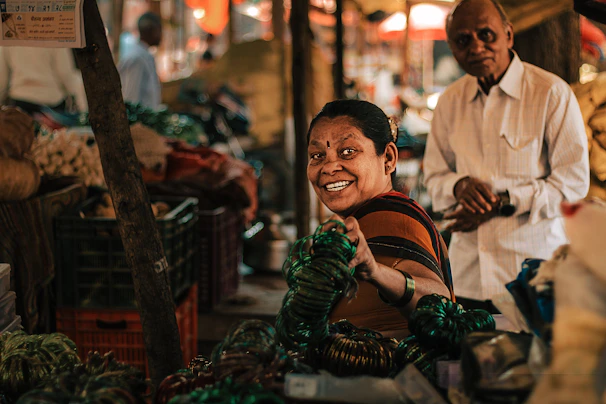 Damayanti and her spouse warmly welcoming customers at a local market stall filled with their products.