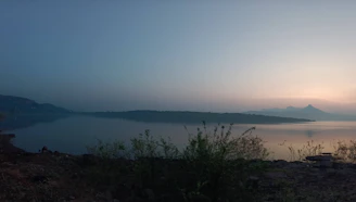 A serene view of Erhai Lake at sunset, with soft golden light reflecting on gentle waves and distant mountains.