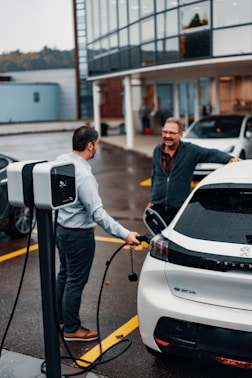 a couple of men standing next to a white electric car