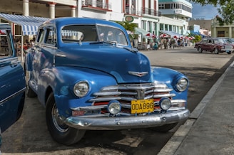 an old blue car parked on the side of the road