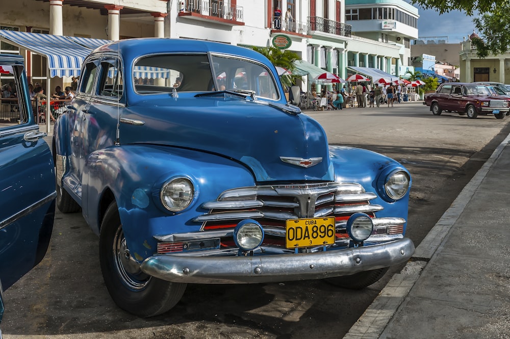 an old blue car parked on the side of the road