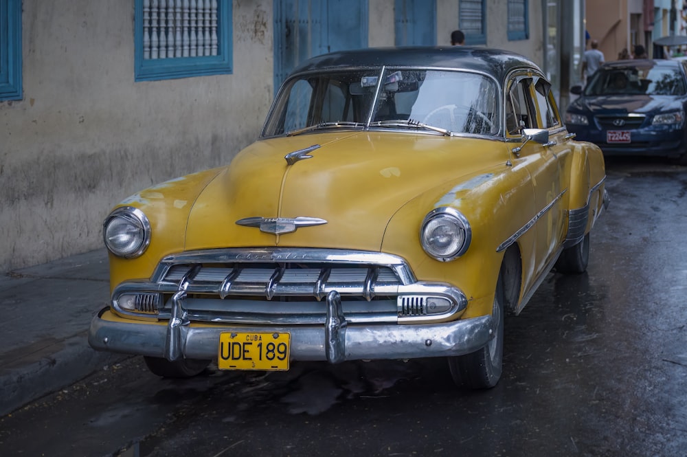 an old yellow car parked on the side of the road
