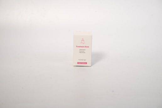 A small rectangular box with a white background, displaying text related to acne treatment. The box has pink text on the front that includes the words 'Treatment Acne'. The surface is smooth and the background is a neutral, light cream color.