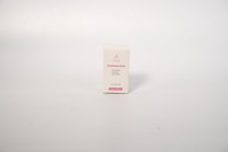 A small rectangular box with a white background, displaying text related to acne treatment. The box has pink text on the front that includes the words 'Treatment Acne'. The surface is smooth and the background is a neutral, light cream color.