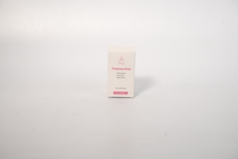 A small rectangular box with a white background, displaying text related to acne treatment. The box has pink text on the front that includes the words 'Treatment Acne'. The surface is smooth and the background is a neutral, light cream color.