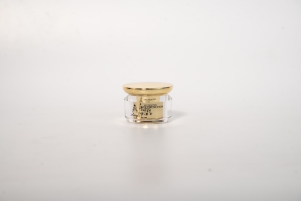 Elegant jar of organic argan cream with a minimalist white and gold label, placed on a white marble background.