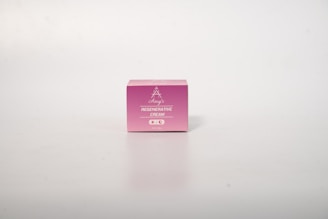 A small, pink box of regenerative cream stands on a plain, light background. The box has simple branding with white text.