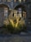 A decorative installation featuring illuminated wireframe reindeer sculptures surrounded by evergreen trees, set against an ornate, historical building facade with arched windows and stone walls. The reindeers are adorned with warm, glowing lights, creating a festive atmosphere.