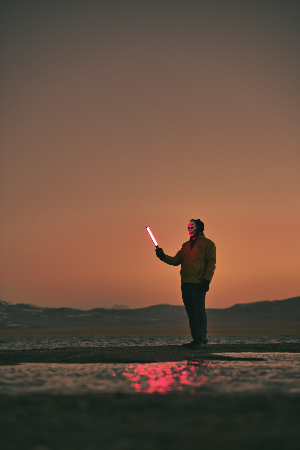 a man standing on a beach holding a light saber