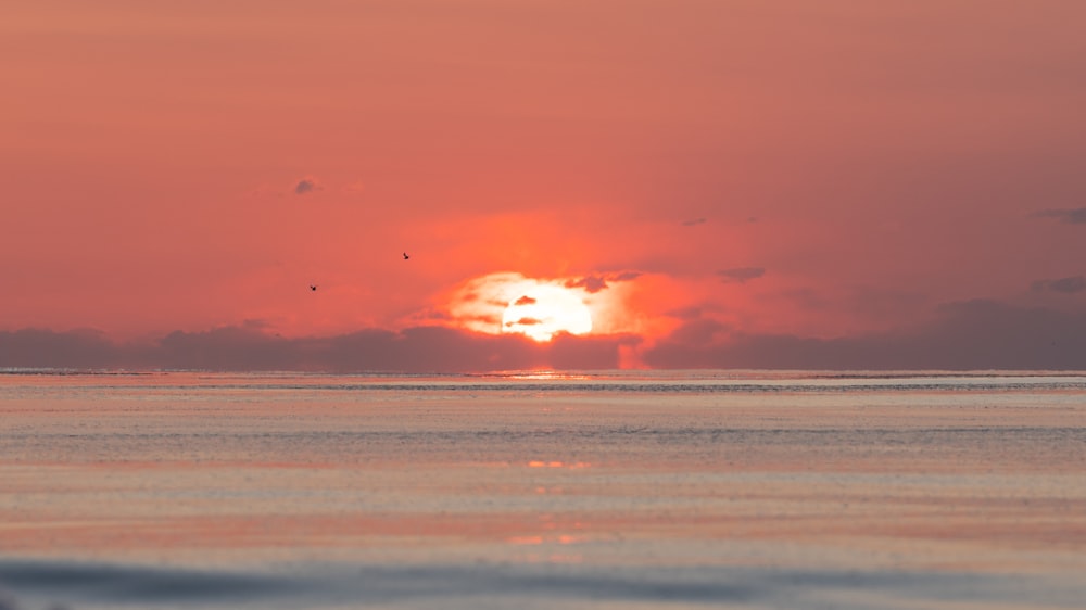 the sun is setting over the ocean on a cloudy day