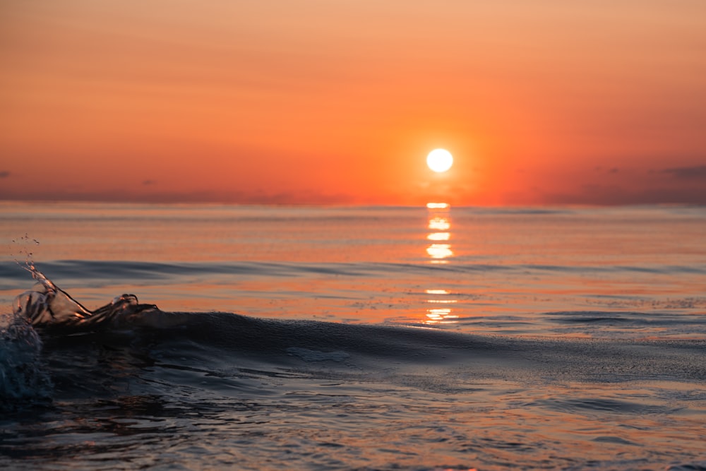 the sun is setting over the ocean with a boat in the water