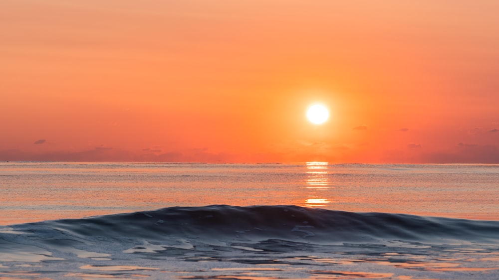 the sun is setting over the ocean with a wave in the foreground