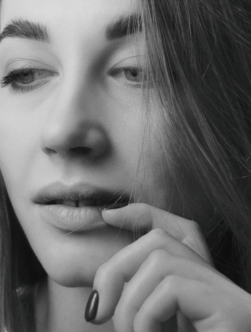 A black and white close-up portrait of a woman with soft natural light highlighting her thoughtful expression.