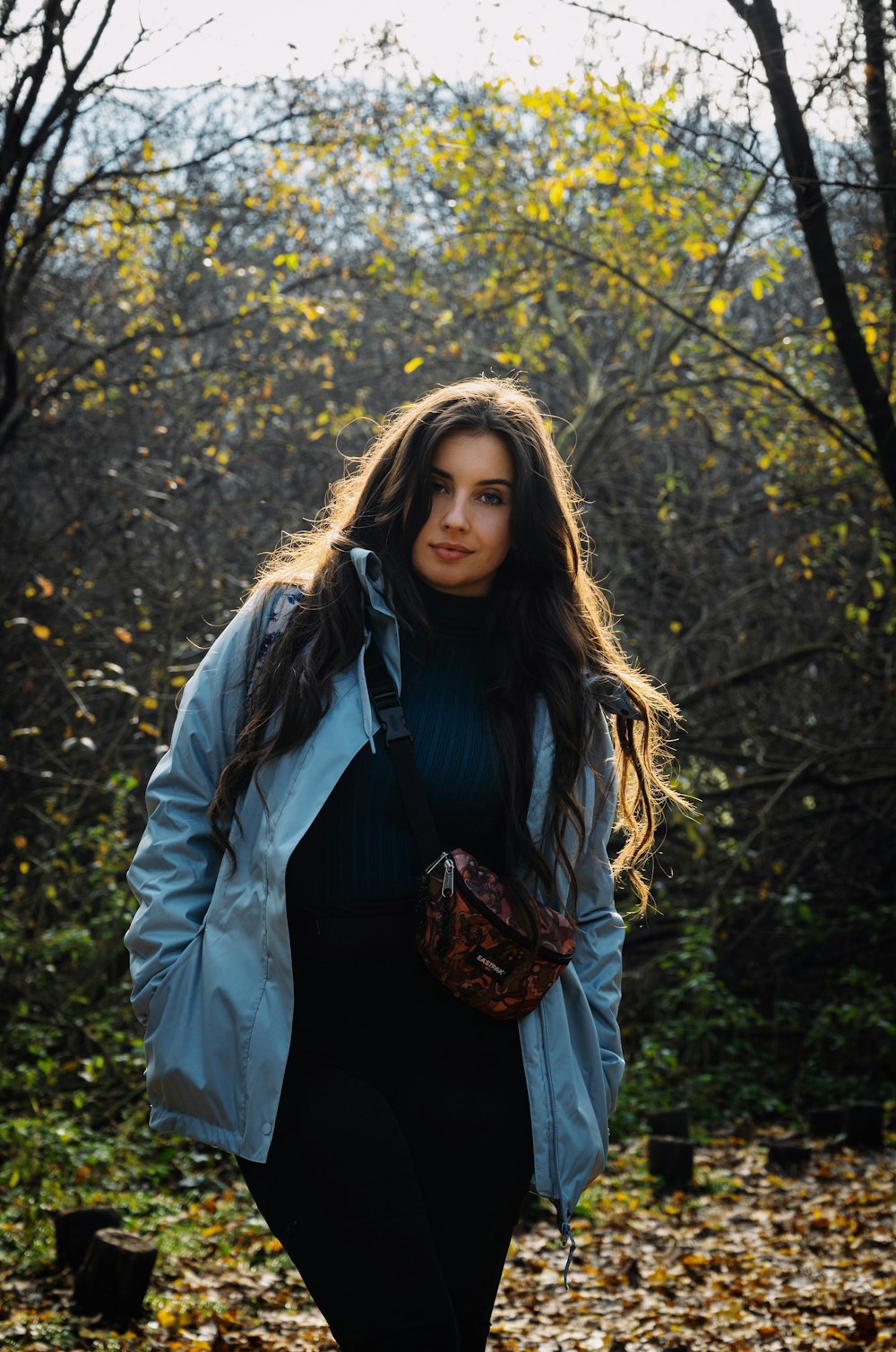 a woman in a blue jacket is walking through the woods