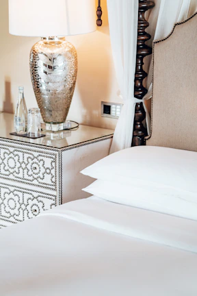 Elegant nightstand with marble top and gold legs beside a plush bed.