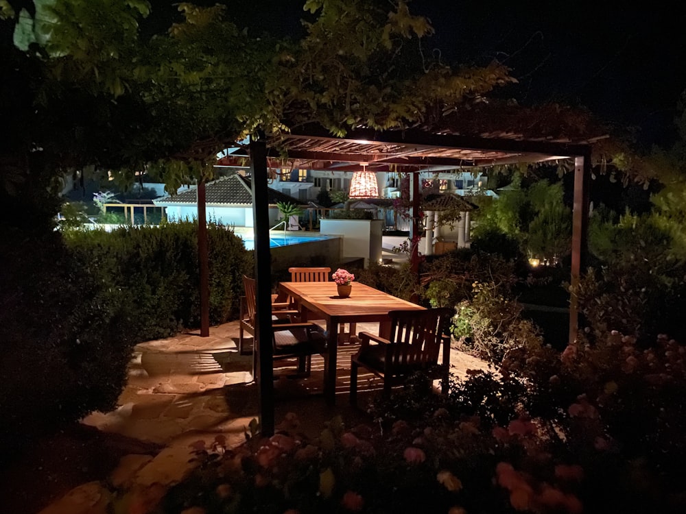a wooden table and chairs under a gazebo at night