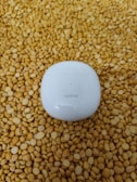 A white Realme earbud case is placed on a surface covered with numerous yellow lentils.