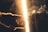 A hand is extended holding a cigarette against a bright, glowing light. Smoke swirls around, creating a hazy atmosphere. Particles appear to be floating in the air, adding to the moodiness of the scene.