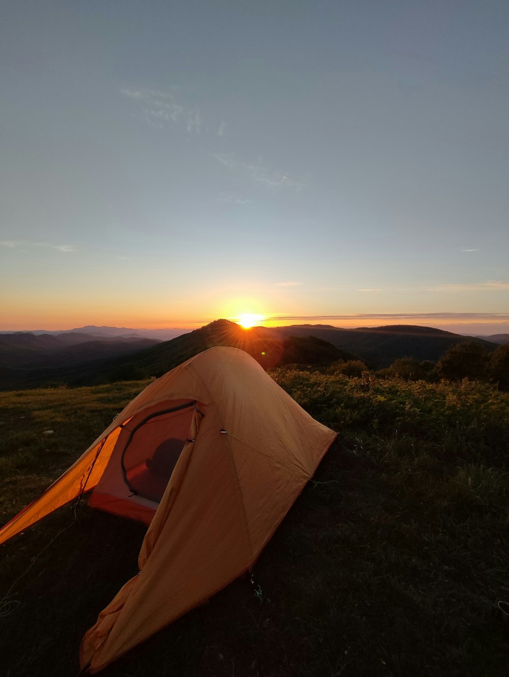 a tent pitched up in the grass with the sun setting in the background