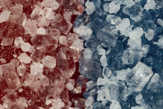 The image contains a close-up view of crystalline structures in varying shades of red and blue. The crystals appear to be irregularly shaped and densely packed together, creating a textured and detailed surface.