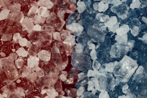 The image contains a close-up view of crystalline structures in varying shades of red and blue. The crystals appear to be irregularly shaped and densely packed together, creating a textured and detailed surface.