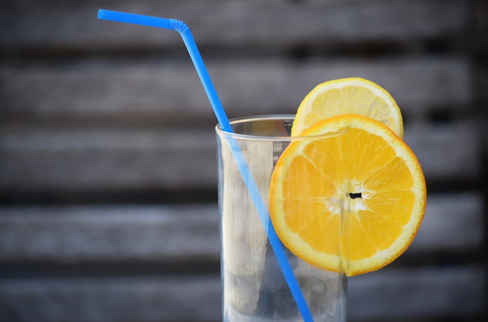 a glass with a blue straw and a half of an orange