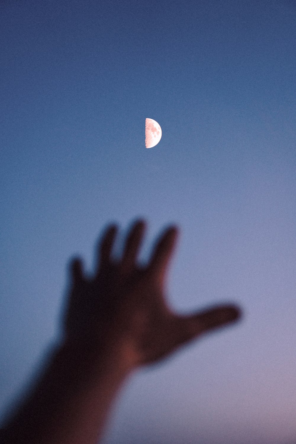 a hand reaching up to a half moon in the sky