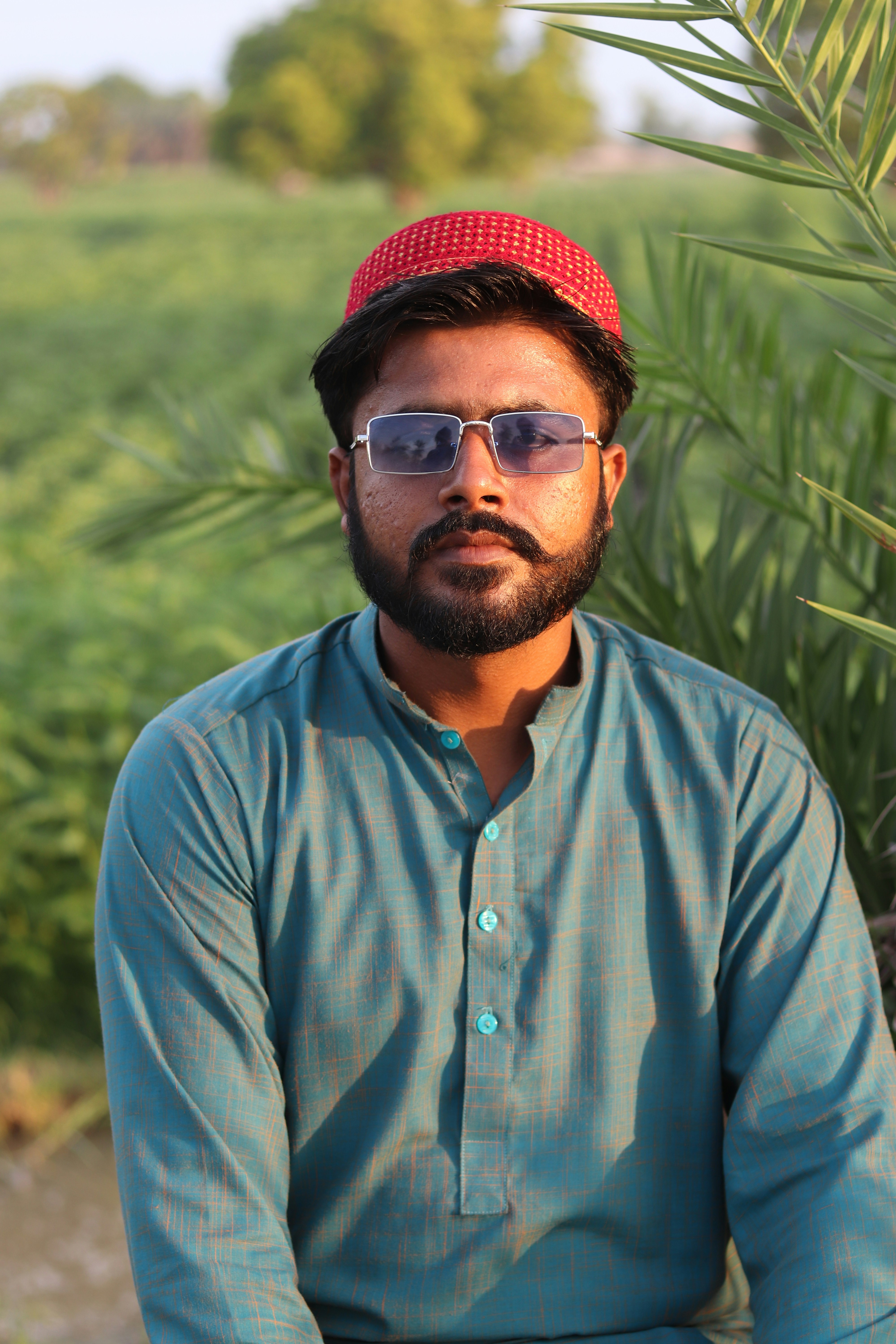 a man with a red hat and sunglasses sitting in front of a palm tree