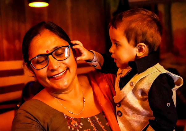 A smiling volunteer gently fitting eyeglasses on a young child in a bright community center.