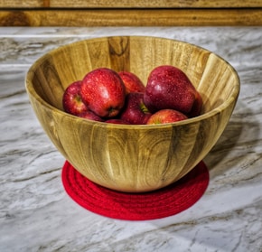 a wooden bowl filled with red apples on top of a counter