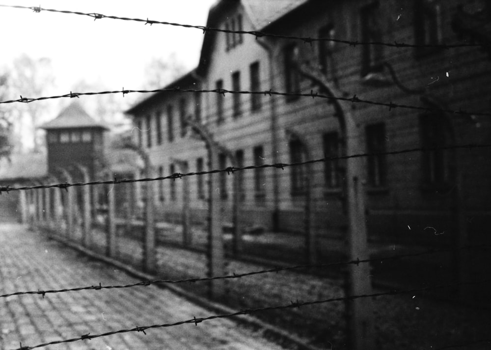 a black and white photo of a building behind a barbed wire fence