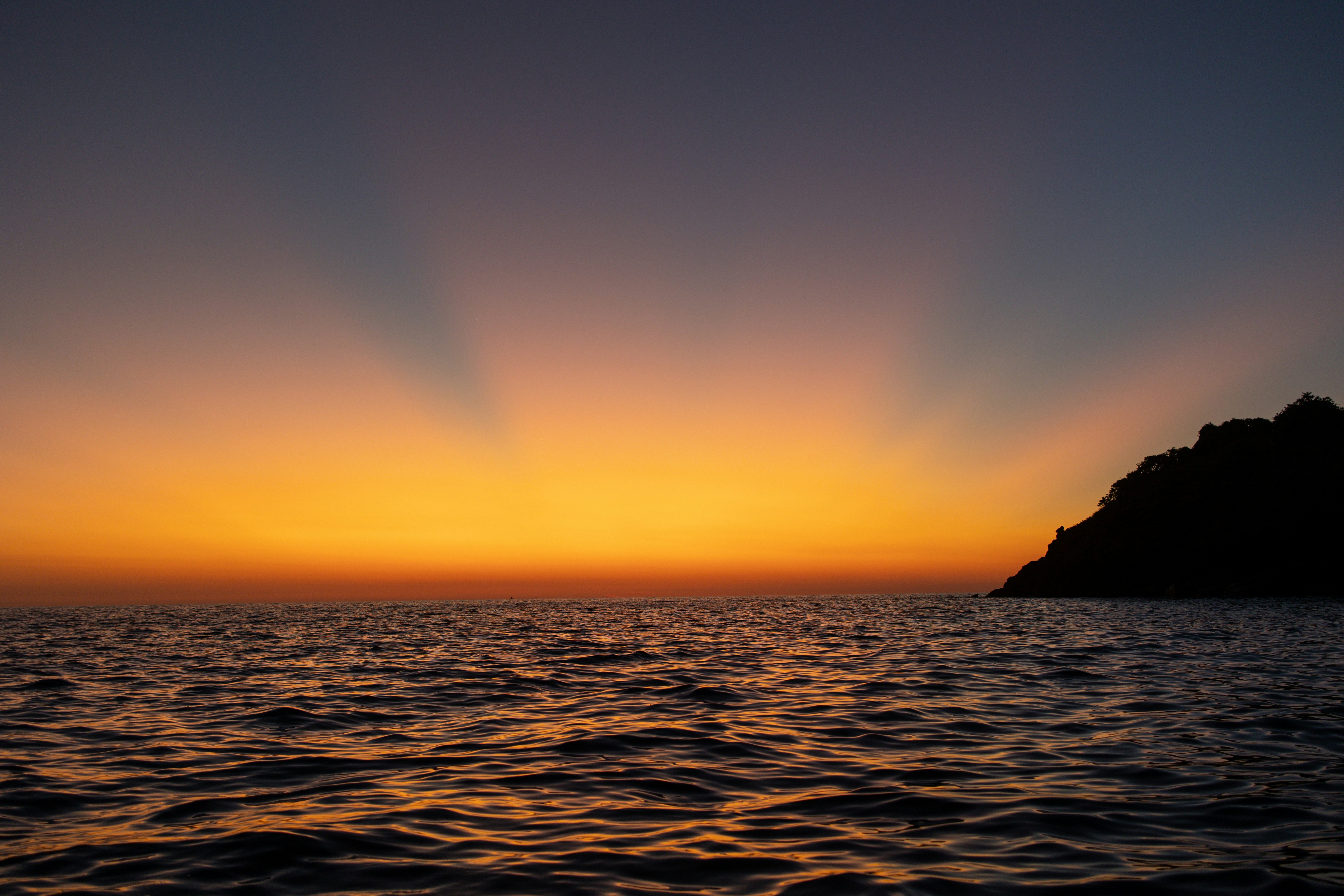 the sun is setting over the ocean with a small island in the distance