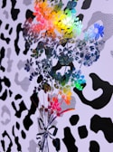 Colorful floral patterns overlap with a black and white abstract design reminiscent of animal prints. The floral pattern includes vibrant hues such as blue, green, yellow, red, and orange, creating a dynamic contrast with the monochrome background.