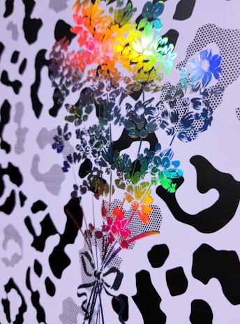 Colorful floral patterns overlap with a black and white abstract design reminiscent of animal prints. The floral pattern includes vibrant hues such as blue, green, yellow, red, and orange, creating a dynamic contrast with the monochrome background.