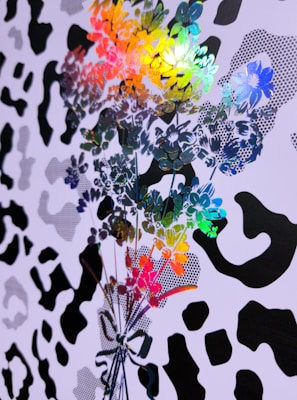 Colorful floral patterns overlap with a black and white abstract design reminiscent of animal prints. The floral pattern includes vibrant hues such as blue, green, yellow, red, and orange, creating a dynamic contrast with the monochrome background.