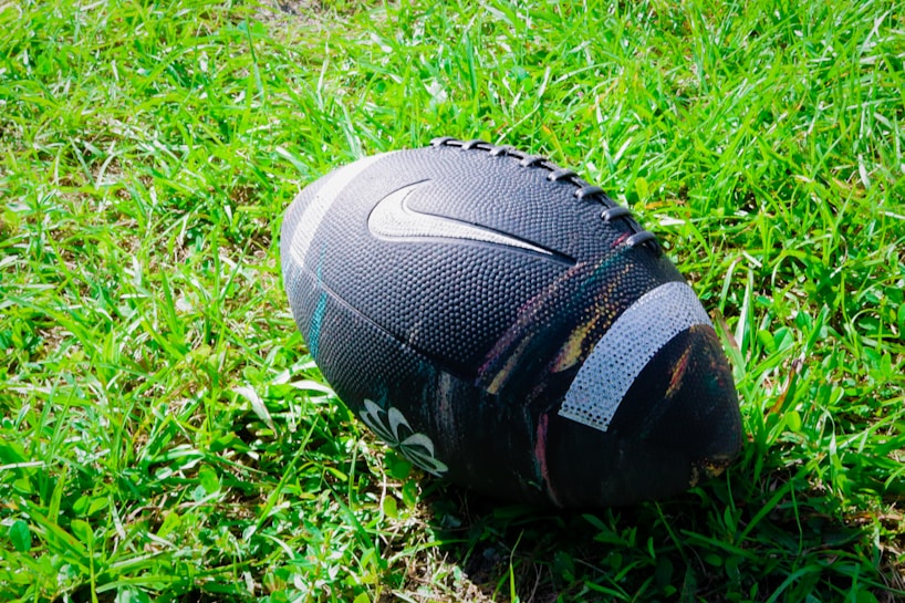 A black football with a textured surface is resting on a field of green grass. The ball features a prominent logo.