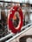 A bright orange lifebuoy is attached to a metallic railing, with some ropes hanging from it. The background features a blurred body of water and tall, dry reeds or grass. The lifebuoy has visible markings on it, including numbers and a label.