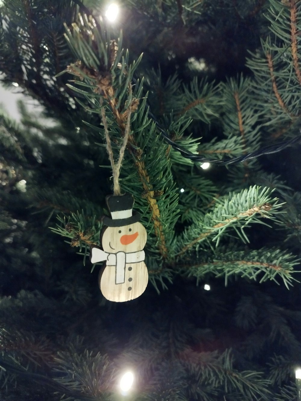 a wooden snowman ornament hanging from a christmas tree