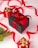 A collection of neatly wrapped gift boxes in various sizes, predominantly featuring red and black wrapping paired with gold accents and ribbons. A black box with a red ribbon is placed centrally, accompanied by smaller red boxes adorned with golden decorations. Bright red ribbon loops artistically across the background, and a sprig of evergreen adds a festive touch.