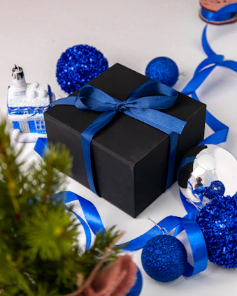 A beautifully arranged gift box with textured wrapping and delicate ribbons, surrounded by festive decorations.
