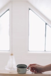 A serene Parisian café scene bathed in soft morning light, with a woman gently holding a coffee cup, embodying calm and elegance.