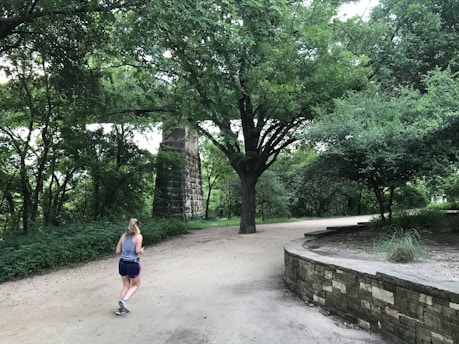 A woman jogging on a scenic trail surrounded by lush greenery and sunlight.